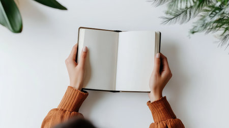 Woman holding a notebook with empty pages on a white table, viewed from the top, perfect for highlighting a clean and fresh workspaceの素材