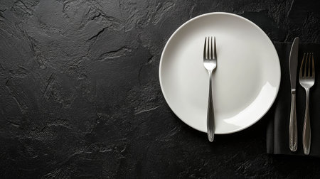 Flat lay of a clean white plate and polished cutlery on a black table surface, ideal for a clean and professional presentation with text spaceの素材