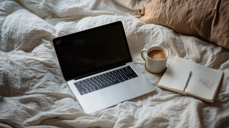 A top view of an open laptop on a bed, with a cup of coffee and a notebook, creating a cozy work-from-home environment.の素材