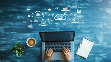 A person typing on a laptop with a coffee cup and notepad on the side, connected to cloud services, top viewの素材