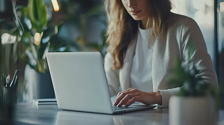 Businesswoman working on a laptop in a stylish, minimalist office, with focus on her hands typingの素材