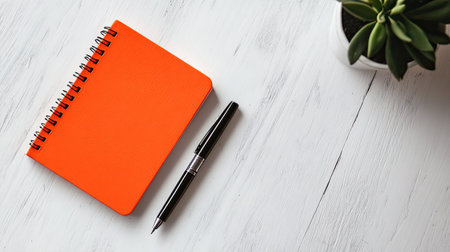 A clean, minimal desk setup with a bright orange notebook and a single penの素材