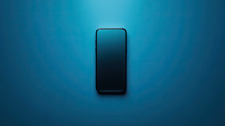 Minimalist blue background featuring a sleek black smartphone, centered and reflecting lightの素材