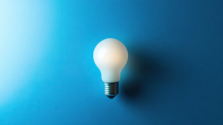 Blue background with a single white lightbulb, centered and softly glowingの素材