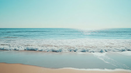 A serene beach with light blue waves gently lapping at the shore under a clear skyの素材