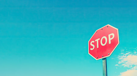 A close-up of a red stop sign against a bright blue skyの素材