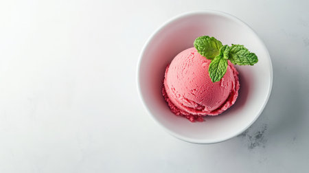 A single scoop of raspberry sorbet in a white bowl, garnished with fresh mint leaves, on a minimalist background.の素材