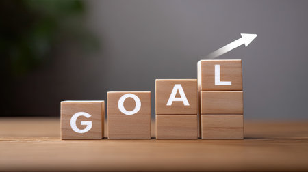 This image showcases wooden blocks spelling the word "GOAL," with an ascending arrow emphasizing progress and achievement in personal and professional growth.の素材