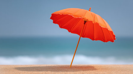 A vibrant orange beach umbrella stands alone on a serene sandy shoreline with ocean waves gently lapping at the coast, evoking a sense of relaxation and summer bliss.の素材