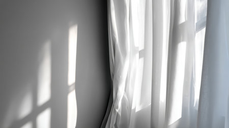 Bright light filters through sheer curtains, casting delicate shadows on a grey wall, creating a calming and serene atmosphere ideal for a cozy indoor space.の素材