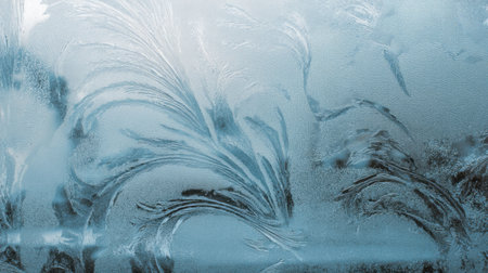 Stunning close-up of frosty window patterns showcasing intricate ice crystals and beautiful designs on the glass surface, evoking a serene winter atmosphere.の素材