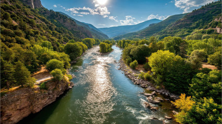 A breathtaking view of a winding river surrounded by vibrant green trees and mountains, illuminated by sunlight against a serene blue sky, perfect for nature lovers.の素材