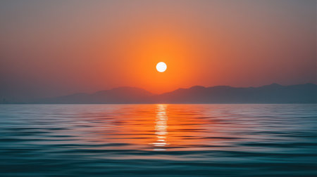 Experience a breathtaking sunset over tranquil waters, with a warm glow illuminating the sky and silhouetted mountains in the background, embodying nature's beauty.の素材