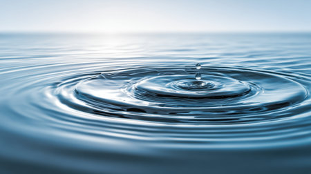 A beautiful close-up view of a water droplet creating ripples on a calm surface under a clear sky. This serene image represents peace and the beauty of nature.の素材