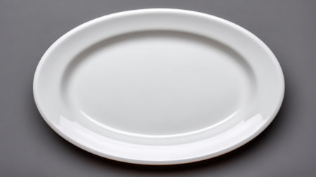 A pristine empty white oval plate set against a gray background perfect for showcasing culinary creations or enhancing dining experiences in various settings.の素材