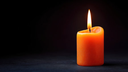 A vibrant orange candle burns brightly, casting a soft glow in a dark setting. This image evokes feelings of warmth, tranquility, and inviting ambiance perfect for relaxation.の素材