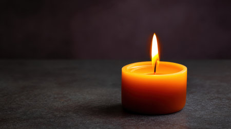 A solitary orange candle with a flickering flame sits on a dark stone surface, radiating warmth and tranquility, ideal for meditation or creating a peaceful ambiance.の素材