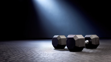 Capture the essence of a workout environment with three black dumbbells subtly illuminated by a spotlight, creating an inspiring atmosphere for fitness enthusiasts.の素材