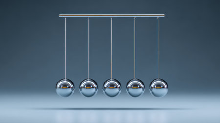 This image depicts five shiny metallic spheres suspended in a perfect line, illustrating the concept of pendulum motion and energy transfer in a clean, modern aesthetic.の素材
