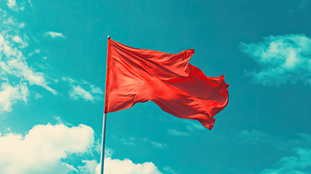 A crimson flag flying proudly in the wind, its vivid color standing out against the bright blue skyの素材