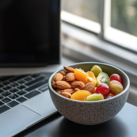 Eating a snack while working, a small bowl of nuts and fruit beside a laptopの素材