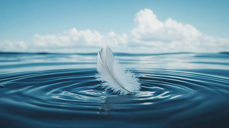 A delicate feather floats gently on the smooth water surface, creating ripples that reflect the serene blue sky and fluffy clouds, evoking tranquility and peace.の素材