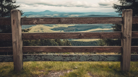 A picturesque view from a wooden fence overlooking expansive green fields and distant hills, capturing the essence of tranquility in nature.の素材