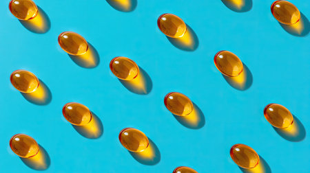 A vibrant flatlay of golden gel capsules arranged on a bright blue background, showcasing health and wellness supplements in a visually appealing way.の素材
