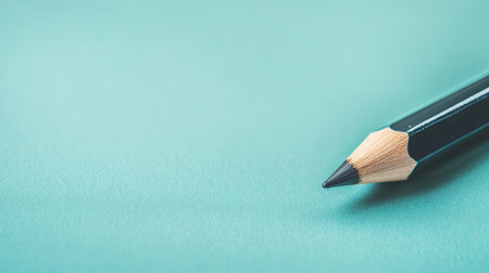 A close-up image of a sharp black pencil resting on a smooth turquoise background. The vibrant color enhances the visual appeal, ideal for creative projects.の素材