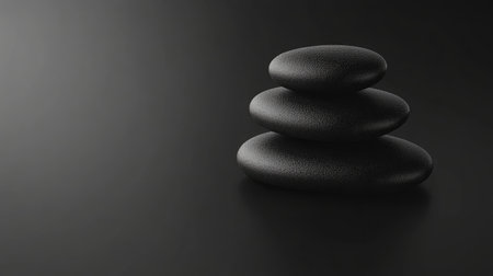 A serene image featuring three smooth black stones stacked elegantly on a dark surface, ideal for themes of relaxation, meditation, and wellness in spa settings.の素材