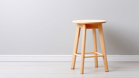 A simple wooden stool stands in front of a light gray wall, embodying minimalist design. The clean lines and natural wood finish enhance modern interior aesthetics.の素材