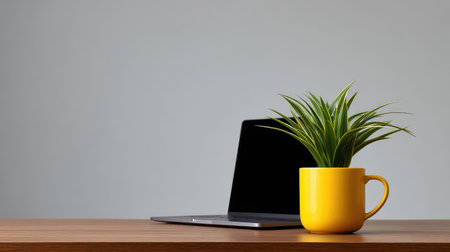 A modern desk setup featuring a sleek laptop beside a bright yellow pot with a green plant, creating a refreshing atmosphere perfect for creativity and productivity.の素材