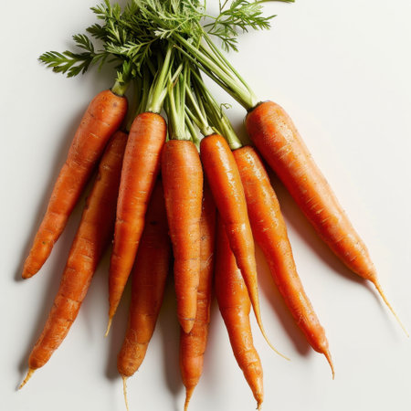 A bunch of fresh orange carrots with green tops displayed against a white background, showcasing their vibrant color and natural texture for healthy culinary inspiration.の素材