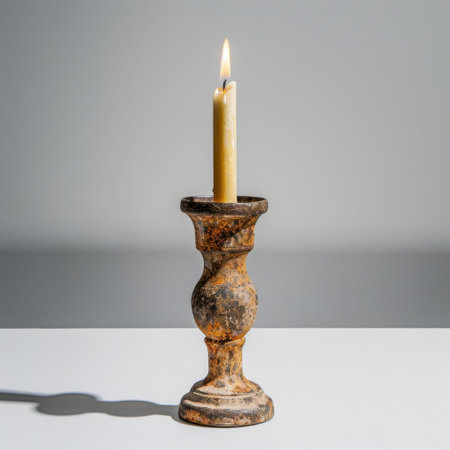 A beautifully aged candle holder featuring a softly lit candle that casts gentle shadows in a minimalist environment, creating a cozy and tranquil atmosphere ideal for interior decor.の素材
