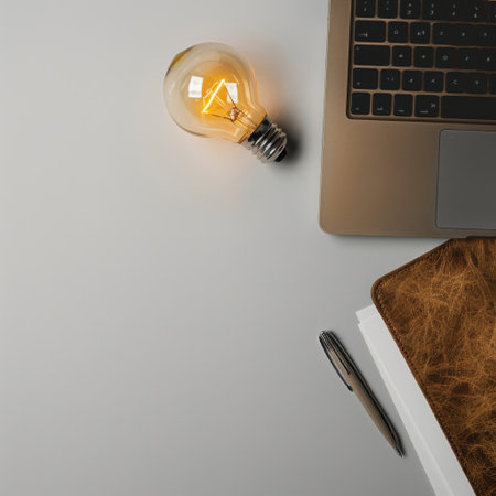 A modern workspace features a laptop, stylish notebook, glowing light bulb, and pen arranged neatly on a wooden desk, ideal for fostering creativity and productivity.の素材
