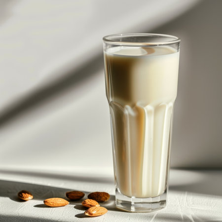 A tall glass of refreshing almond milk stands elegantly on a light surface with almonds scattered nearby, showcasing a healthy and natural beverage choice for all.の素材