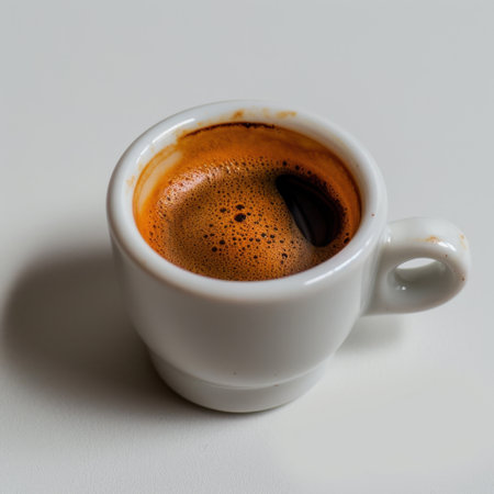 A striking close-up view of freshly brewed espresso coffee in a white ceramic cup, showcasing rich creamy foam and deep brown colors against a minimalist background.の素材