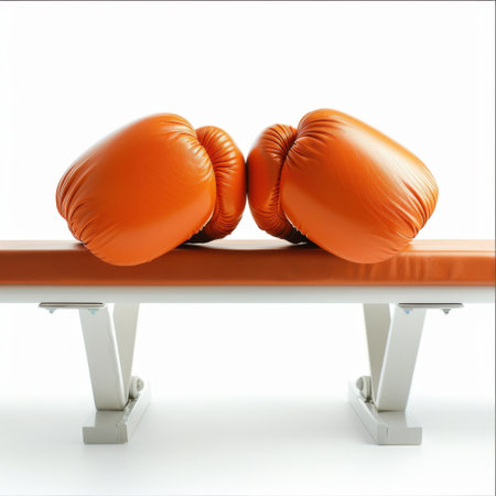 A pair of vibrant orange boxing gloves sit on a sleek bench, reflecting a dedication to fitness and training in a clean, modern gym environment.の素材