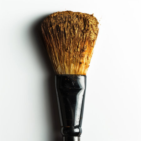 A stunning close-up of a makeup brush with sparkling gold residue set against a pristine white background, perfect for beauty and fashion themes in photography.の素材