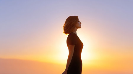 A serene silhouette of a woman with short hair stands against a magnificent sunrise. The scene captures her feelings of freedom and tranquility in nature.の素材