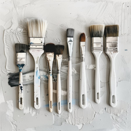 A collection of various paint brushes displayed on a textured white plaster surface. Ideal for artists, crafters, and DIY enthusiasts seeking inspiration and tools.の素材