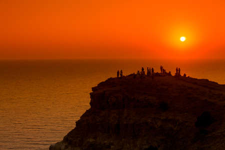People silhouettes on the sunset on the cliff over the seaの写真素材