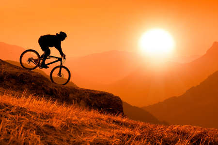 silhouette of downhill mountain bike rider at orange sunsetの写真素材