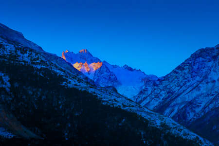 bright sunset over Caucasian mountains peaks in blue dusk