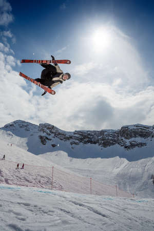 Sochi, Krasnaya Polyana ski resort / Russia - March 25 2020: Freestyle ski rider making a spectacular stunt in mountain snow park, ski crossed, against blue sky, mountains, sun and clouds. Extreme winter sportのeditorial素材