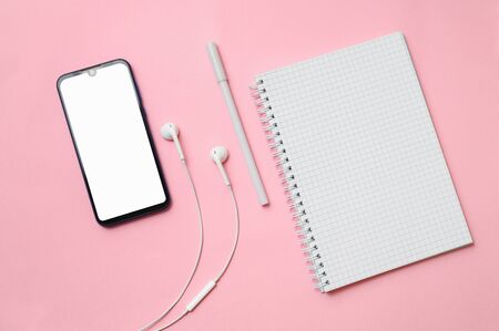 White headphones, a pen, a notebook in a box ismartphone with a white display lie on a pink tableの写真素材