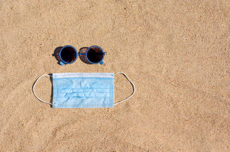 Sunglasses and a medical mask lie on the beach on the sand. view from above. Vacation concept during a pandemic.の写真素材