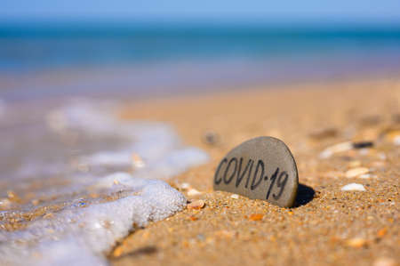 Pebbles with the inscription Covid-19 on the beach by the sea. Sea vacation symbol during the coronavirus epidemic.の写真素材