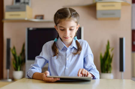 A girl with two pigtails and in a blue shirt is using a tablet at home.の写真素材
