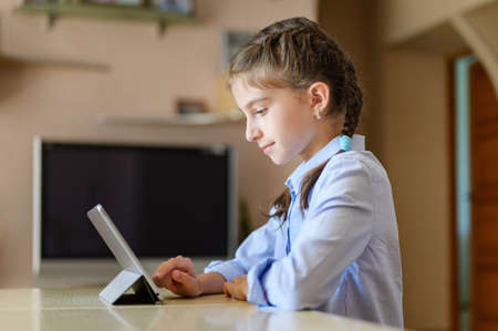 The girl at home sits at a table and uses a tablet.の写真素材